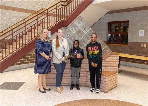 Shadrak Kakule. Grover Cleveland's November Stairclimber, poses with his plaque, family members and school staff.