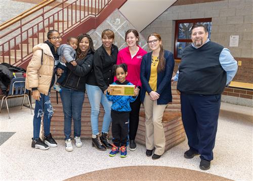 JoAnna Connell's March Stairclimber, Romeo Thompson, posing with his plaque, family members, and school staff.