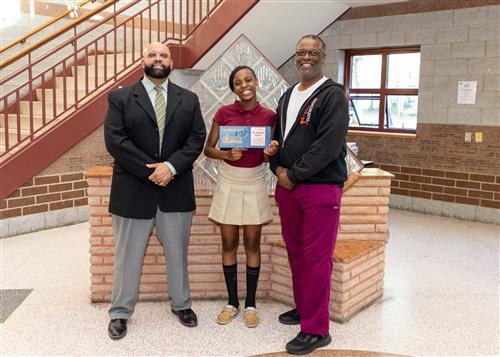 My'Honesty Carter. Eagle's Nest's May Stairclimber, poses with her plaque, a family member, and DEI Coordinator Ken Nickson.