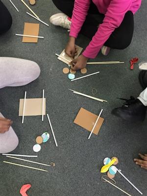 Photo shows part of cardboard used to make paper cars stewn about a carpet, with student hands