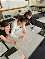 A group of three students huddle over a paper spread out on their desk, at work on a Black History Month project.