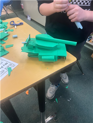 Photo of a student working on what appears to be a kit made up of green pieces that when assembled look like a tank.