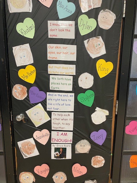 Photo of a door covered with text of "I am Enough" by Grace Byers, along with cutouts of paper hearts with student & teach. 