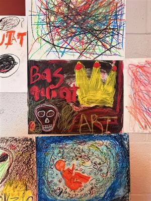 Close up of several student-created artworks displayed in the hallway of East. The art is in the style of Basquiat.