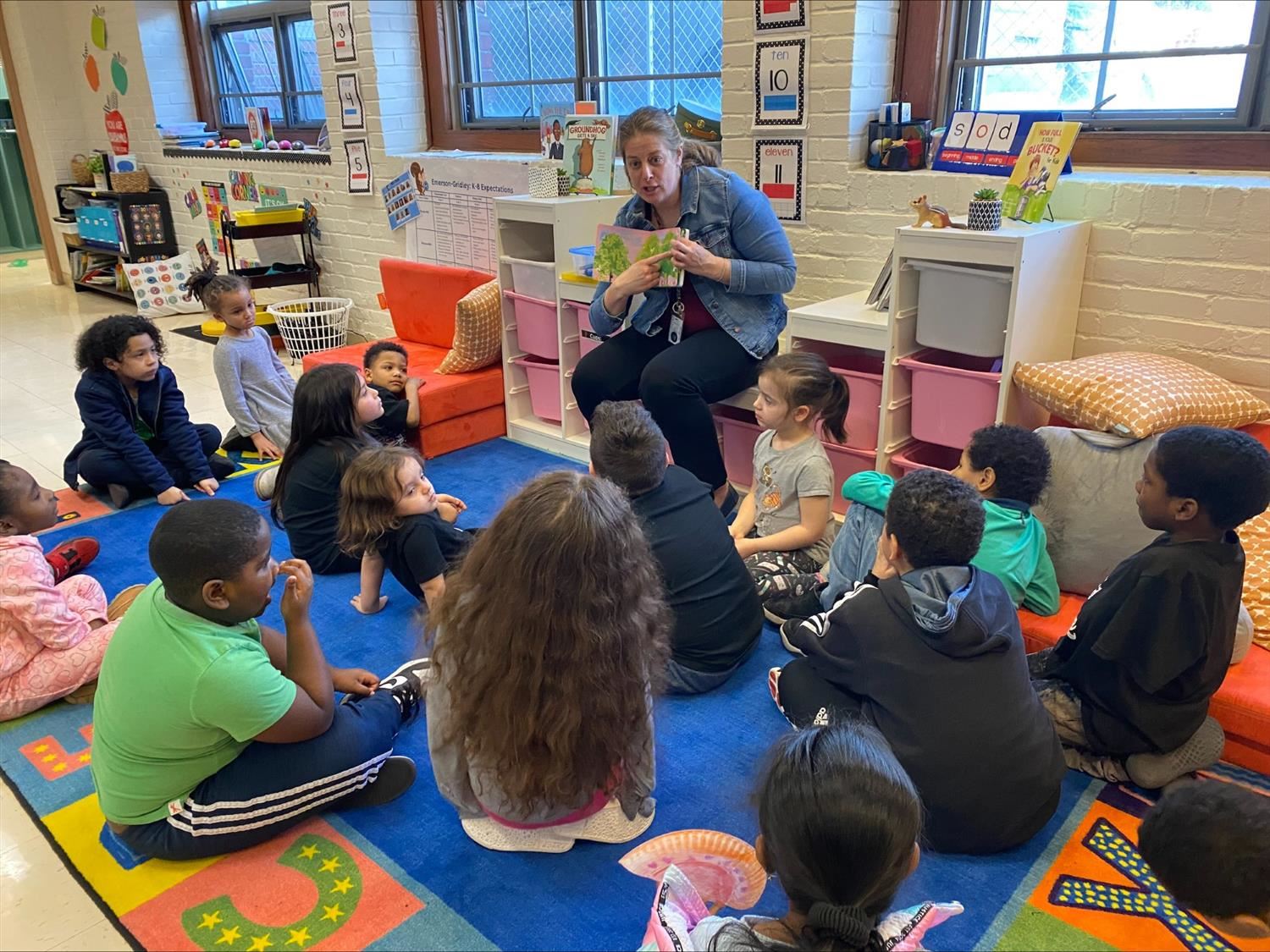 Students sitting on an alphabet area rug with teacher showing pages from the book "What a Wonderful World."