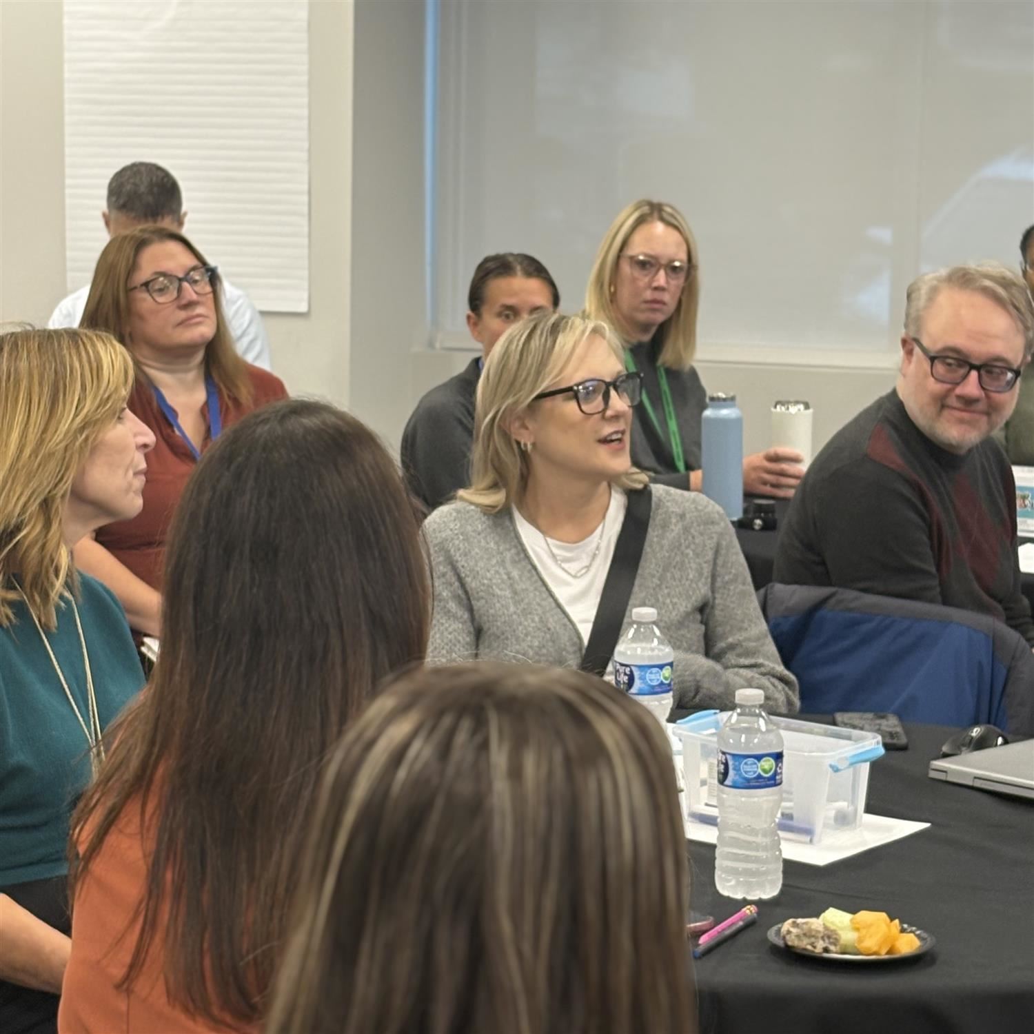 Woman in gray sweater sitting with other people at a round table.